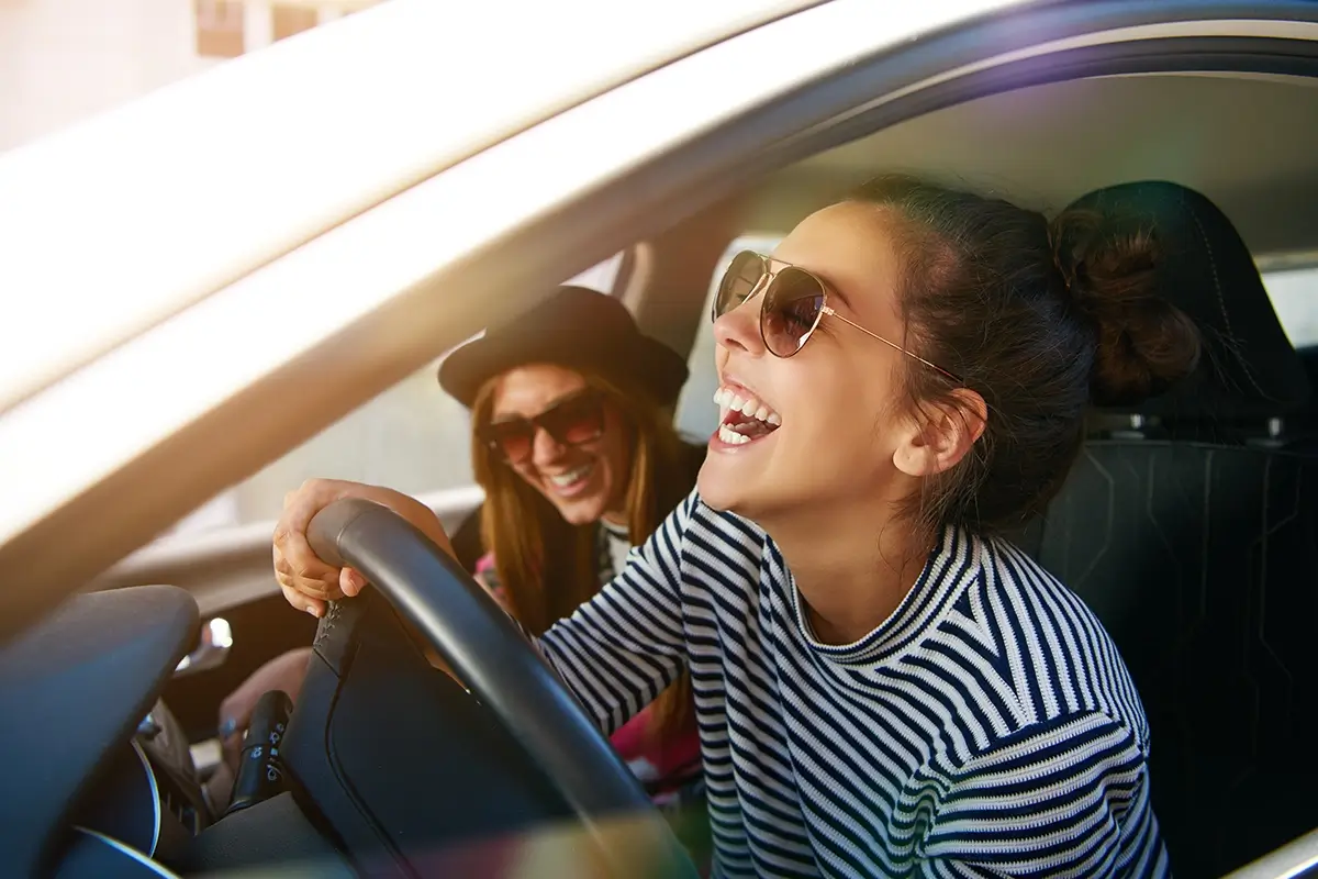 Zwei Personen sitzen im Fahrzeug, die Sonne scheint und sie lachen.
